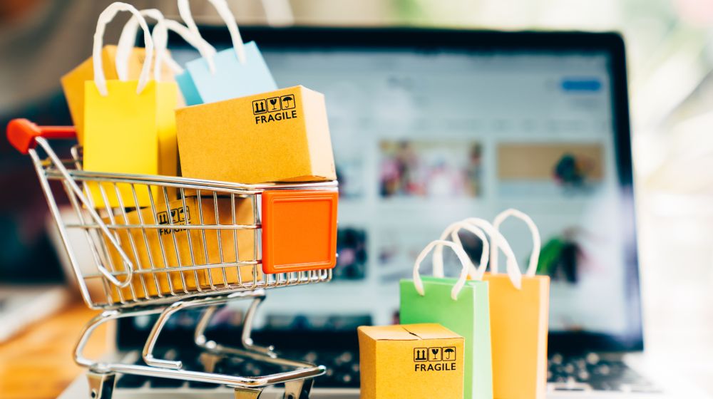 A mini shopping trolley filled with packages in front of a laptop open on an eCommerce website, symbolsing how having the right eCommerce theme can make a difference to sales